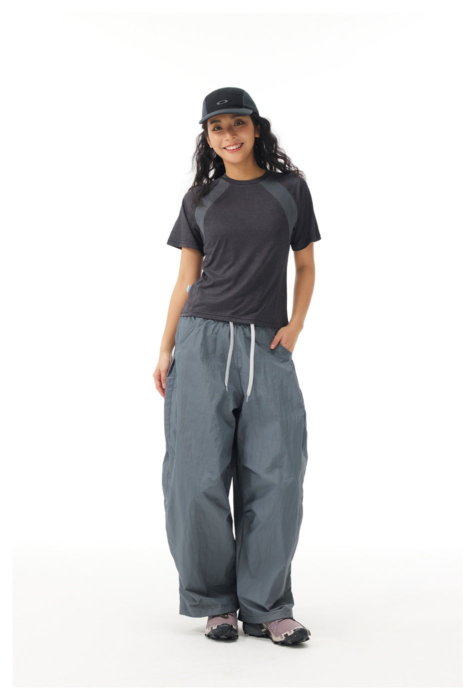 Full-length model wearing a charcoal raglan T-shirt, loose slate-gray drawstring pants, and a black cap.