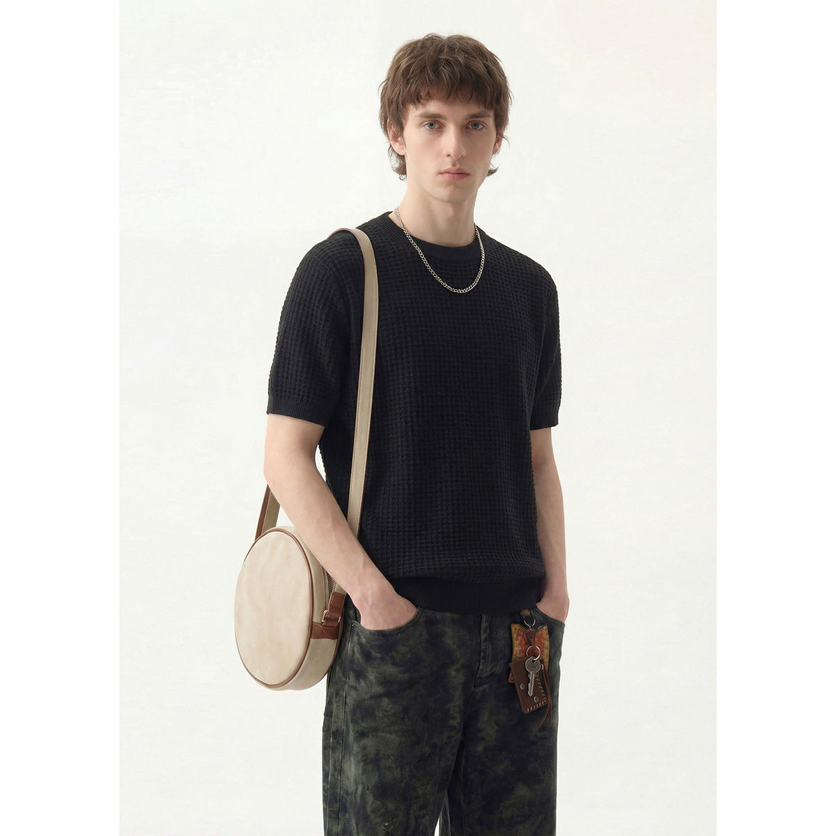 Model wearing a black textured short-sleeve crew-neck shirt with dark patterned trousers.