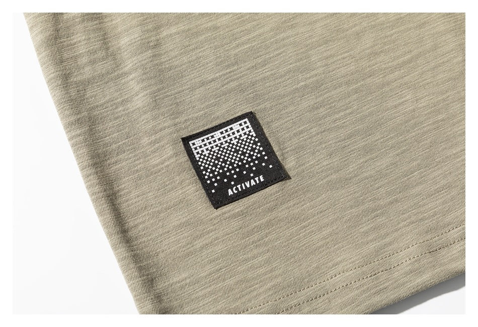 Close-up of a black geometric patch reading “ACTIVATE” on the khaki shirt near the hem.