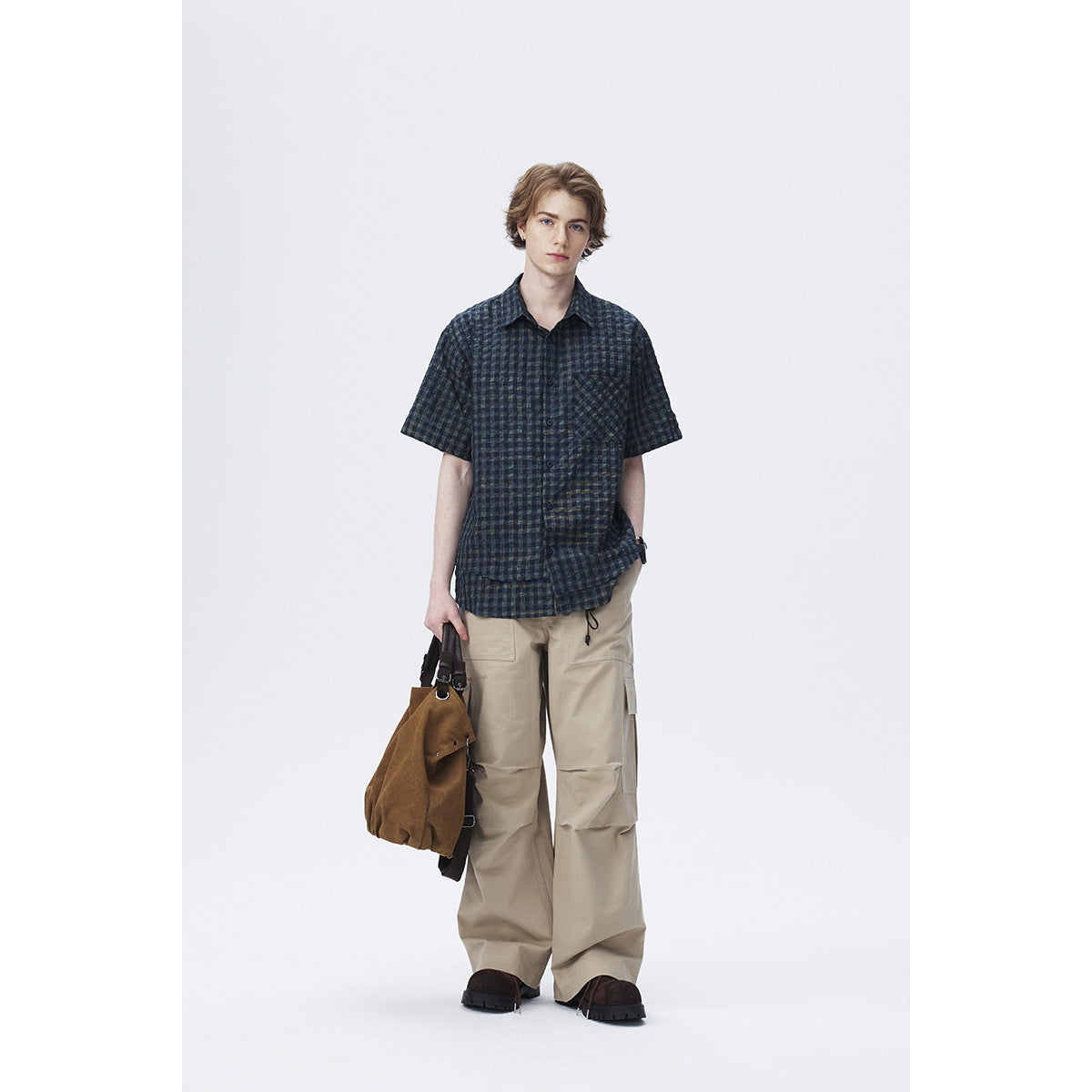 Full-length model wearing a dark navy and green plaid short-sleeve shirt with beige cargo trousers.
