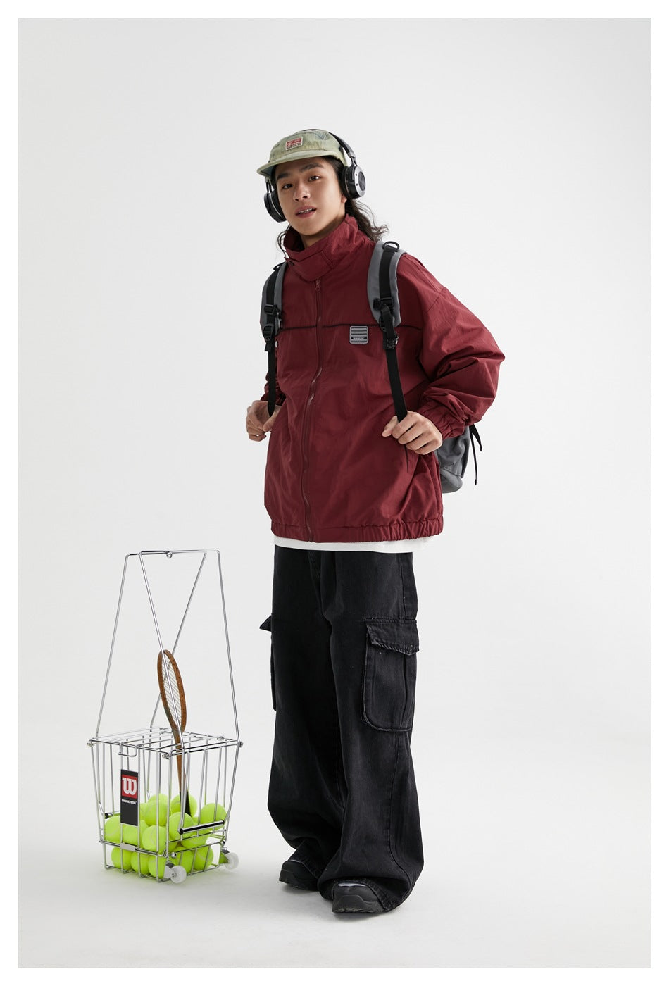 Model wearing a burgundy zip-front jacket with a high collar, black piping and elastic cuffs, styled with black cargo pants.