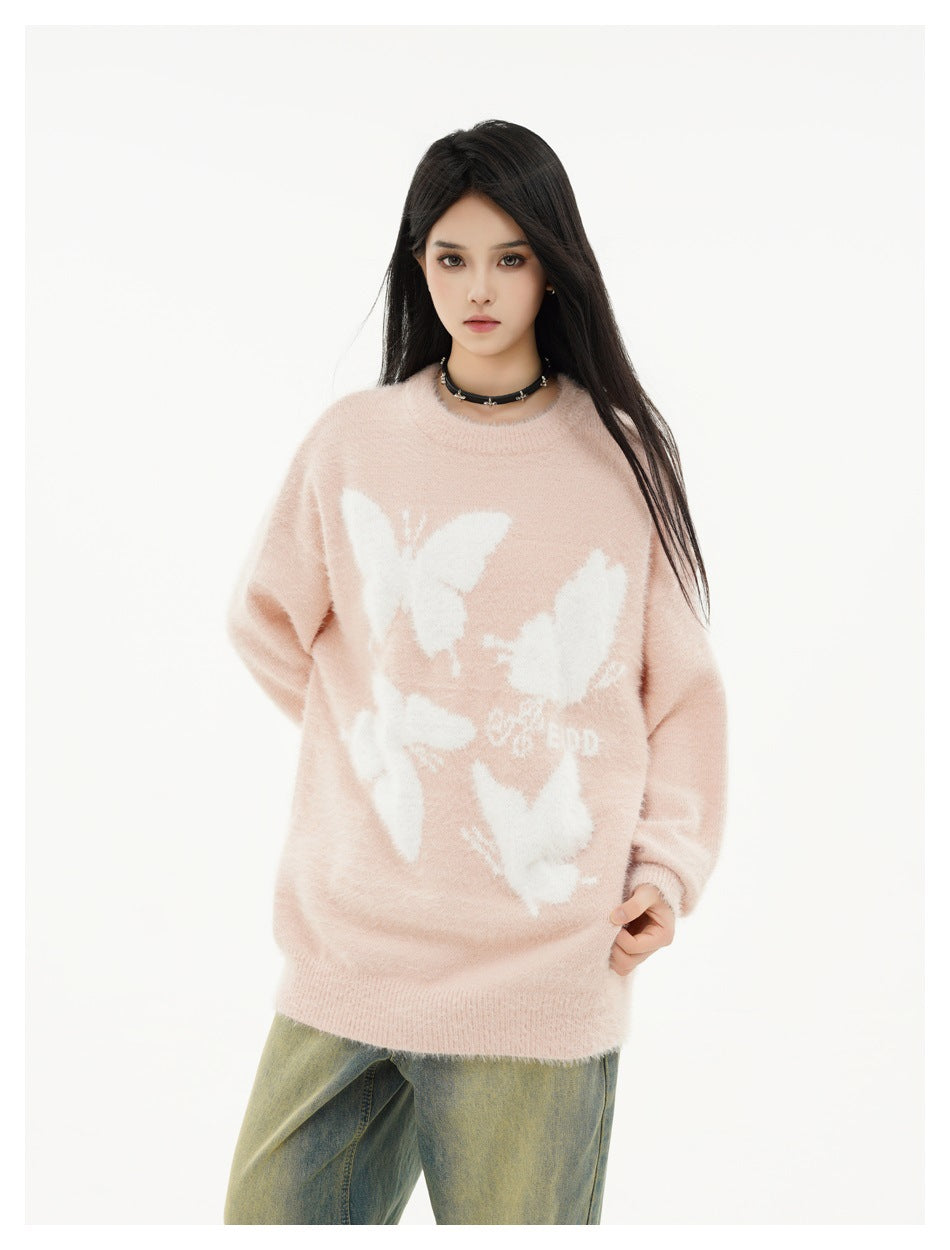 Closer front view of a model wearing a pale pink oversized sweater with white butterfly motifs and ribbed trim.