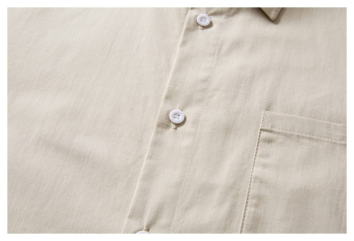 Close-up of an ivory shirt front with white buttons, a chest pocket edge, and part of the collar.