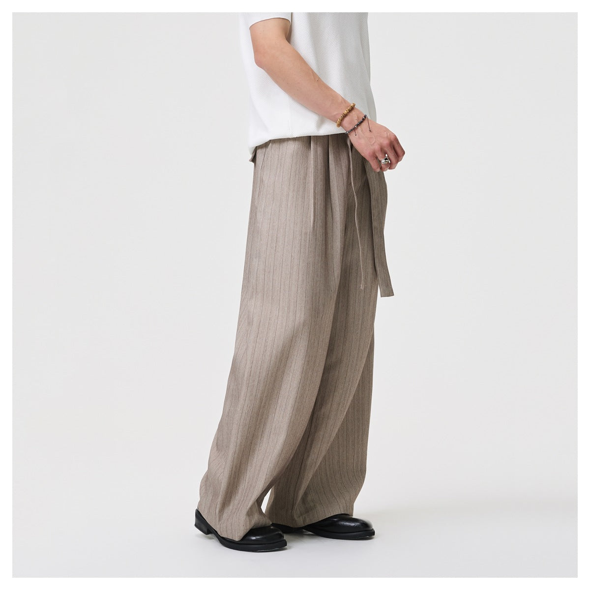 Side view of a model wearing loose taupe-gray pinstriped trousers with a long waist tie.