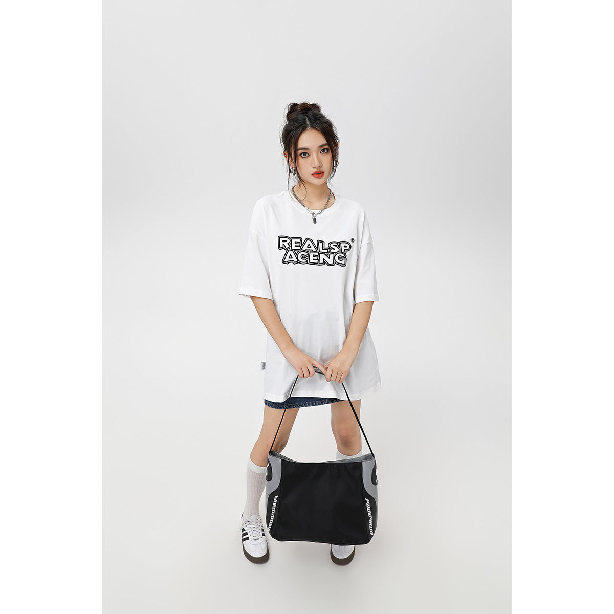 Model wearing an oversized white graphic T-shirt with black chest lettering, denim shorts, knee socks and sneakers.