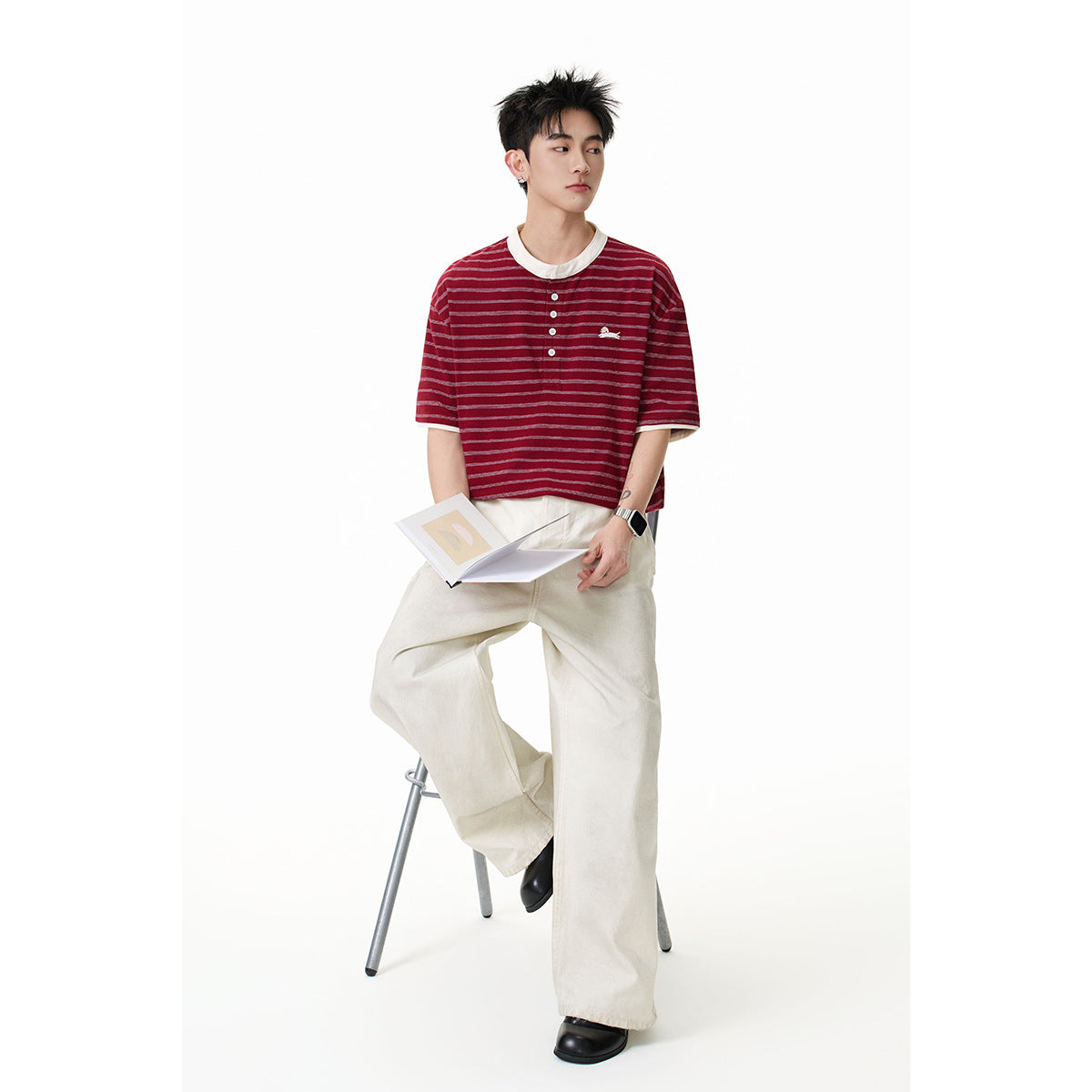 Model wearing a burgundy striped short-sleeve henley with a cream collar and loose ivory trousers.