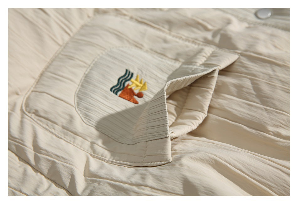 Close-up of a cream garment pocket with colorful embroidered artwork and a ribbed, pleated texture.