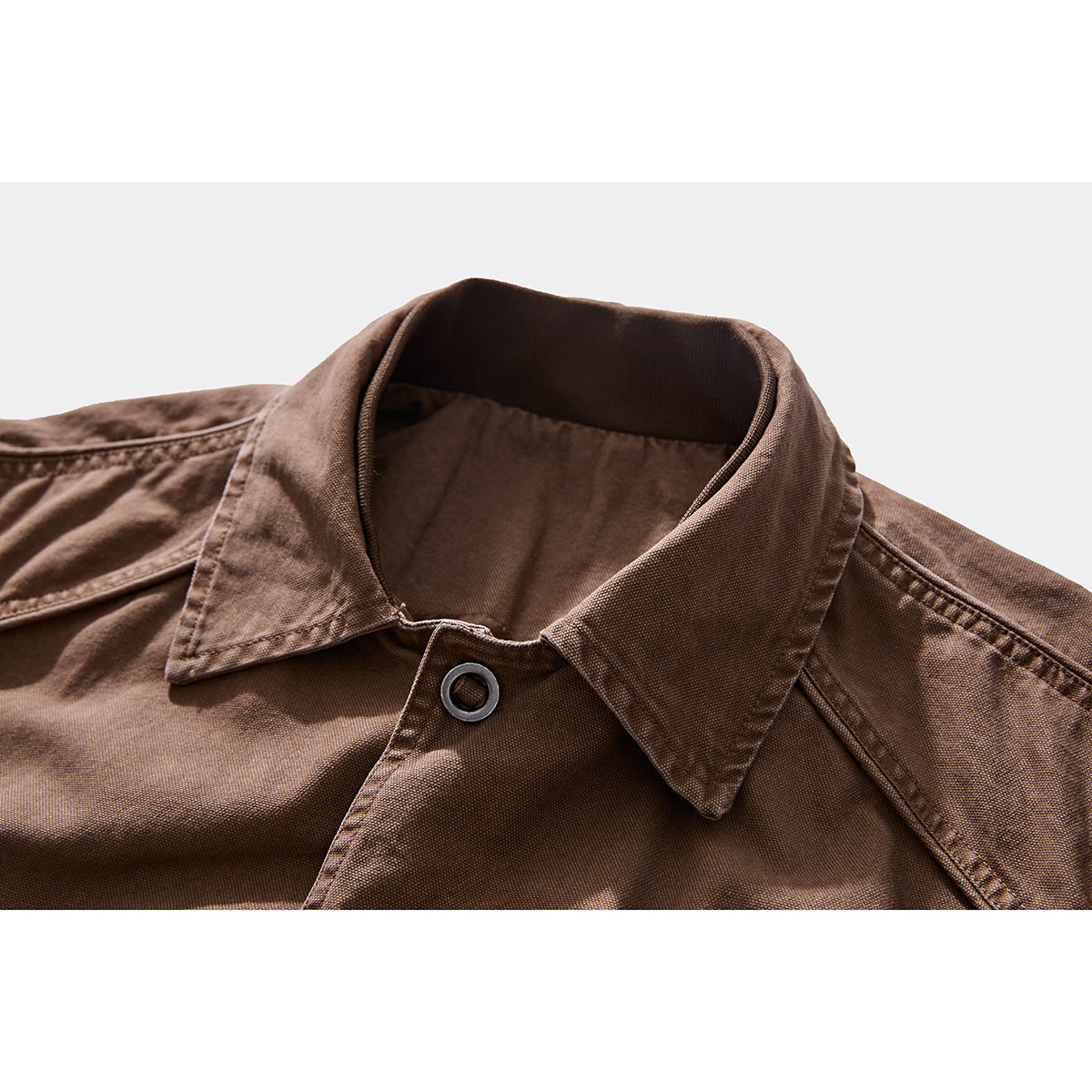 Close-up of a brown jacket's pointed collar, neckline, stitching, and dark ring-style button.