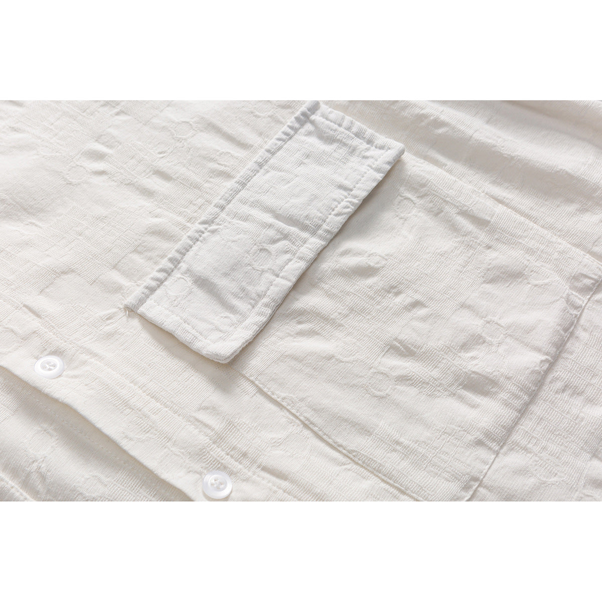 Close-up of a white textured shirt showing its chest pocket, sleeve cuff, and buttons.