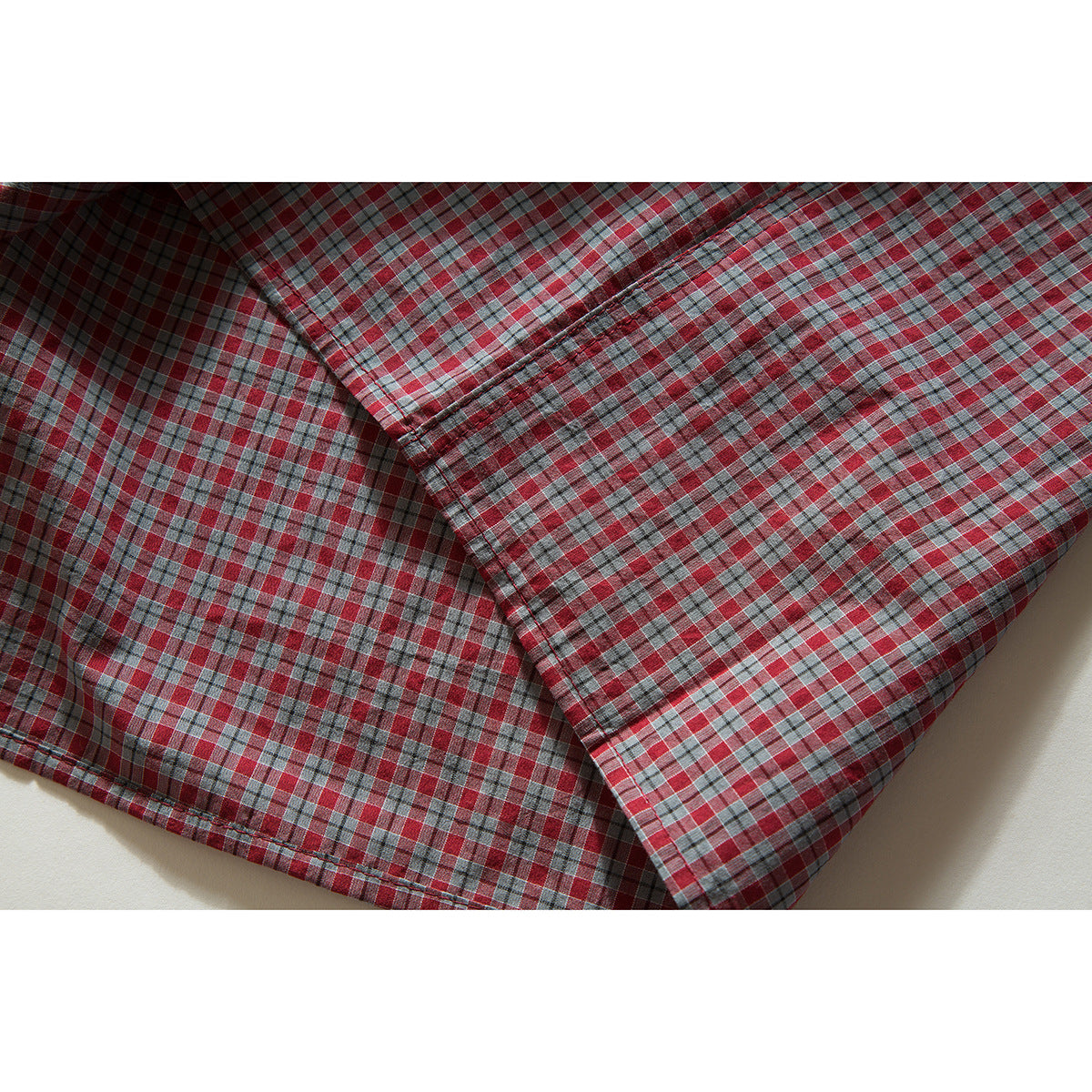 Close-up of a folded sleeve and stitched cuff on a red, gray, and blue plaid shirt.