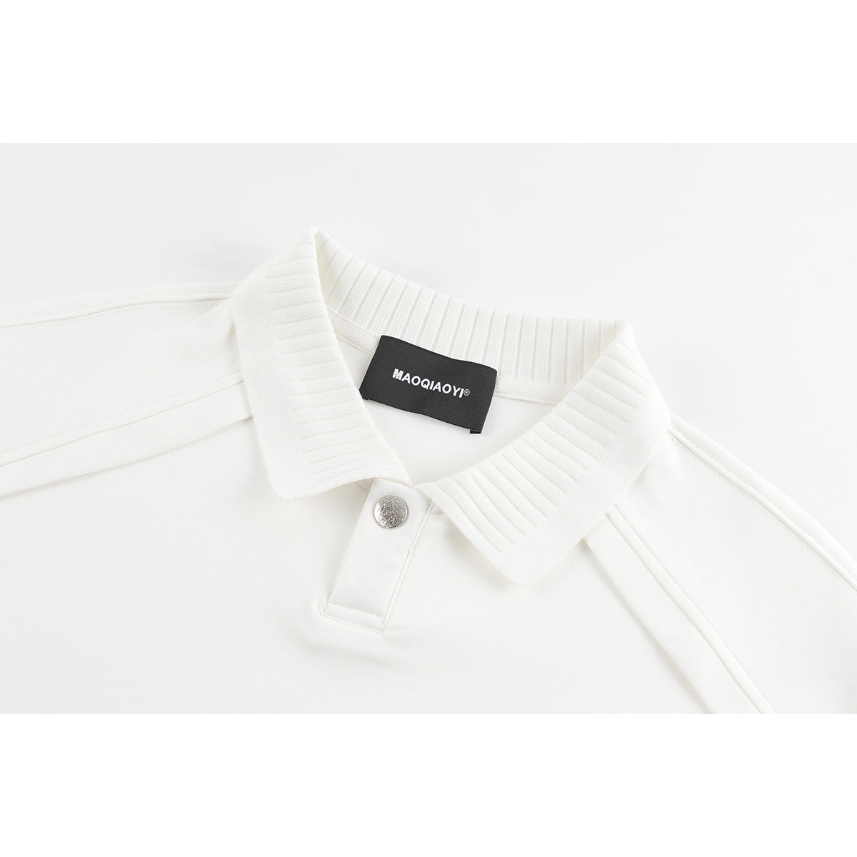 Close-up of a white polo shirt collar with ribbed trim, a silver snap, and a black neck label.