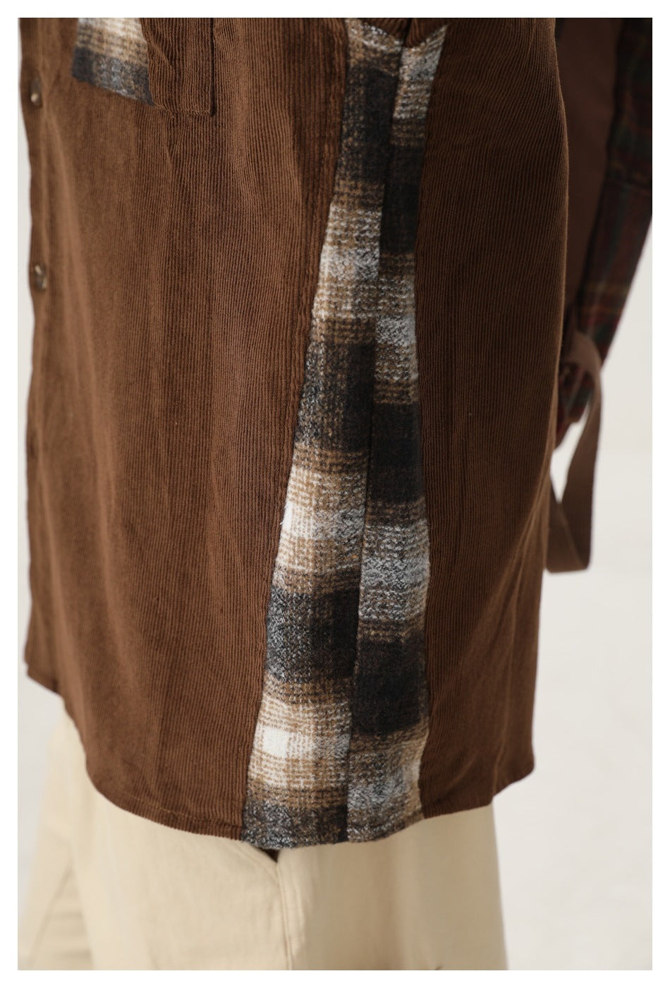 Close-up of a brown corduroy shirt worn with cream trousers, showing a gray, cream and brown plaid side panel.