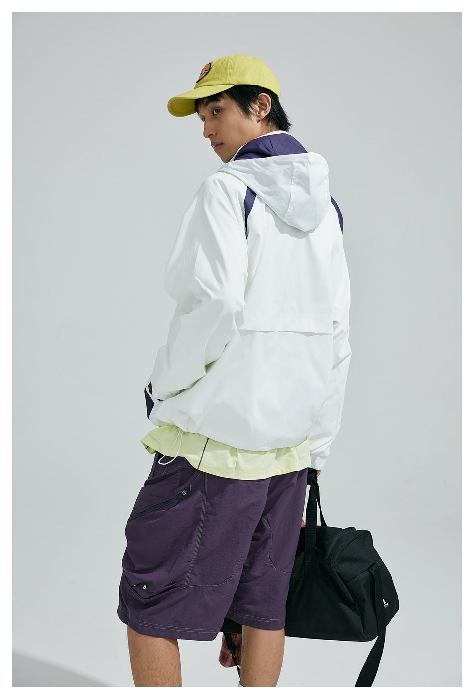 Back view of a model wearing a white hooded jacket with purple accents, paired with purple shorts.