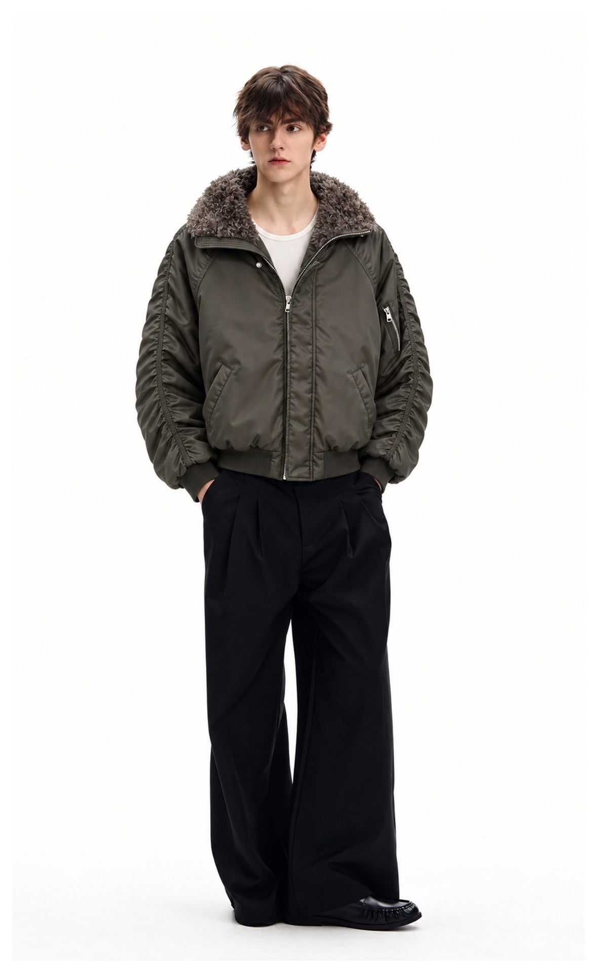 Full-length male model wearing a dark olive bomber jacket with a plush gray collar and black wide-leg trousers.