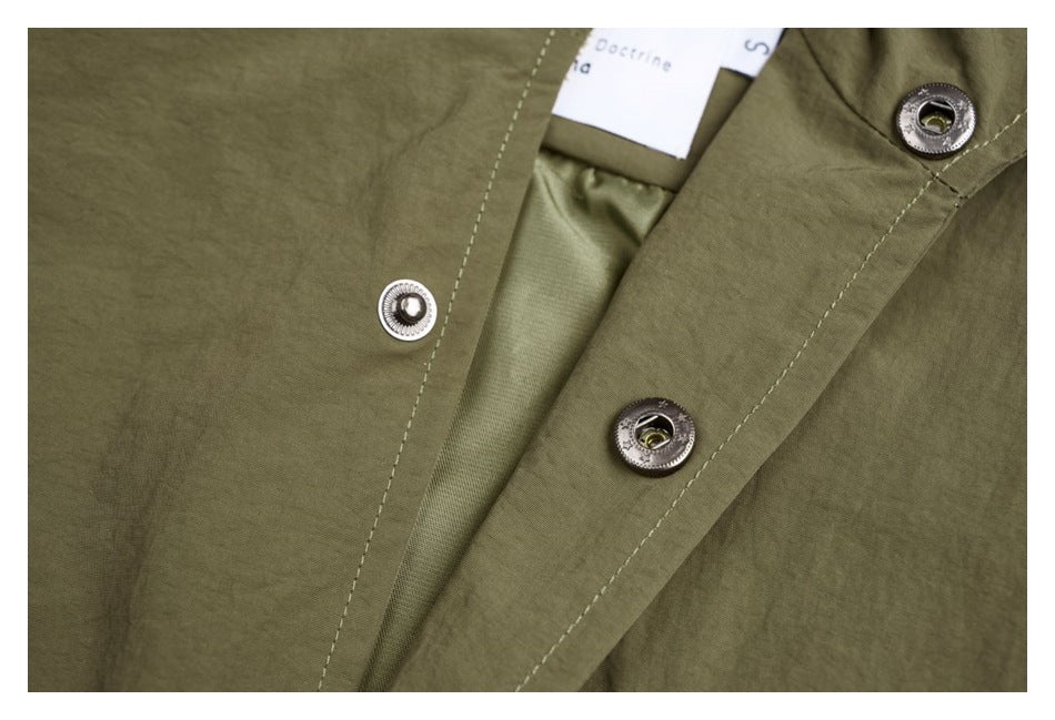 Close-up of the olive jacket's front placket, metal snaps, inner lining and a partially visible white neck label.