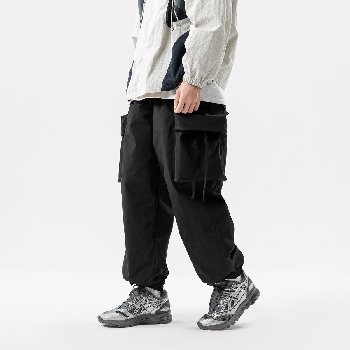 Model wearing black oversized cargo pants with large flap pockets and elastic cuffs, shown from the side.