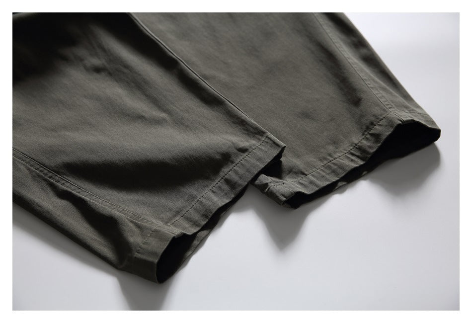 Close-up of the stitched hems on the legs of dark olive-gray pants.