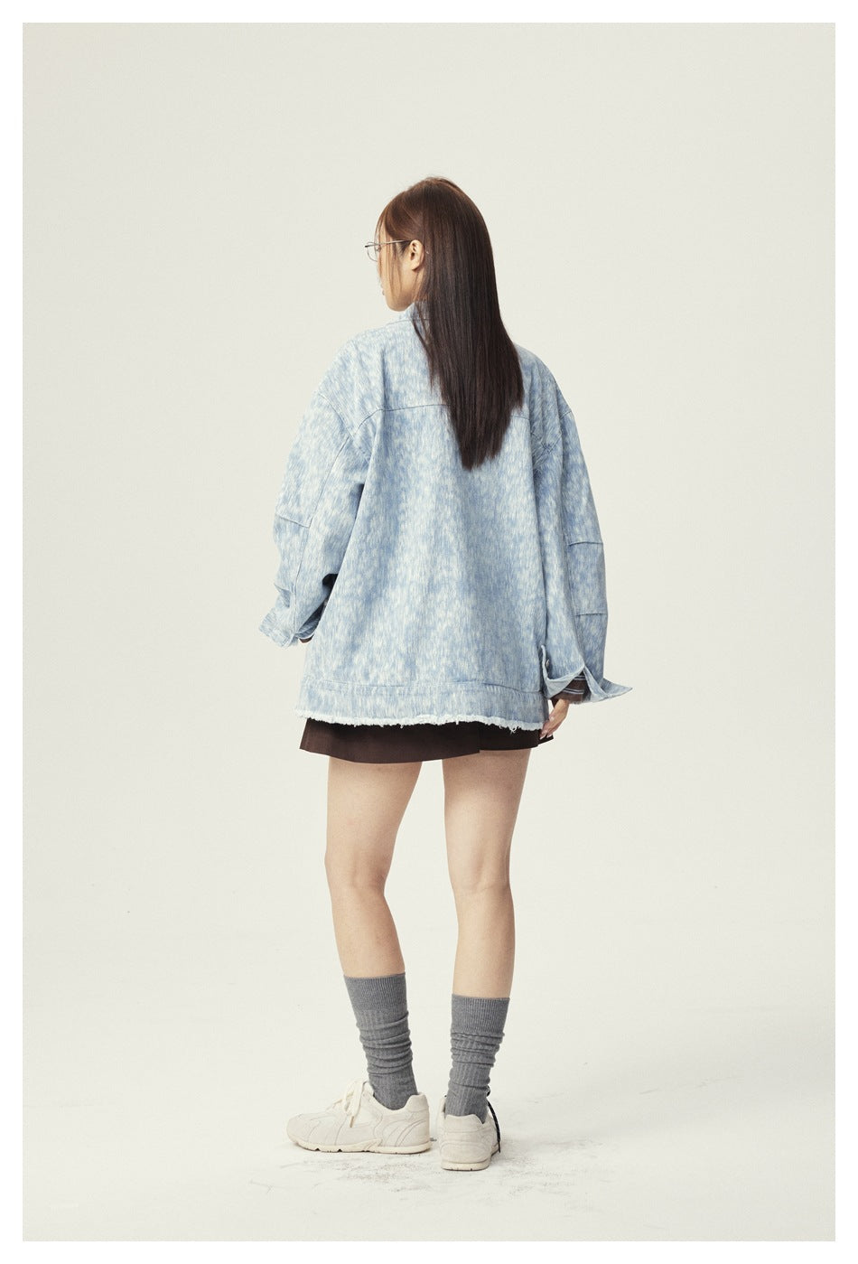 Back view of a model wearing an oversized pale blue mottled jacket with a frayed hem.