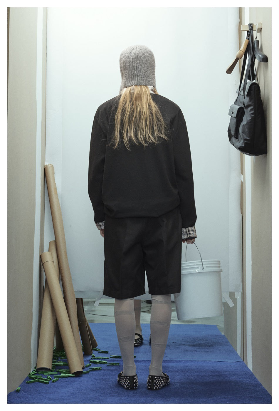 Back view of a model wearing a black long-sleeve top and knee-length shorts with plaid cuffs and gray knee socks.