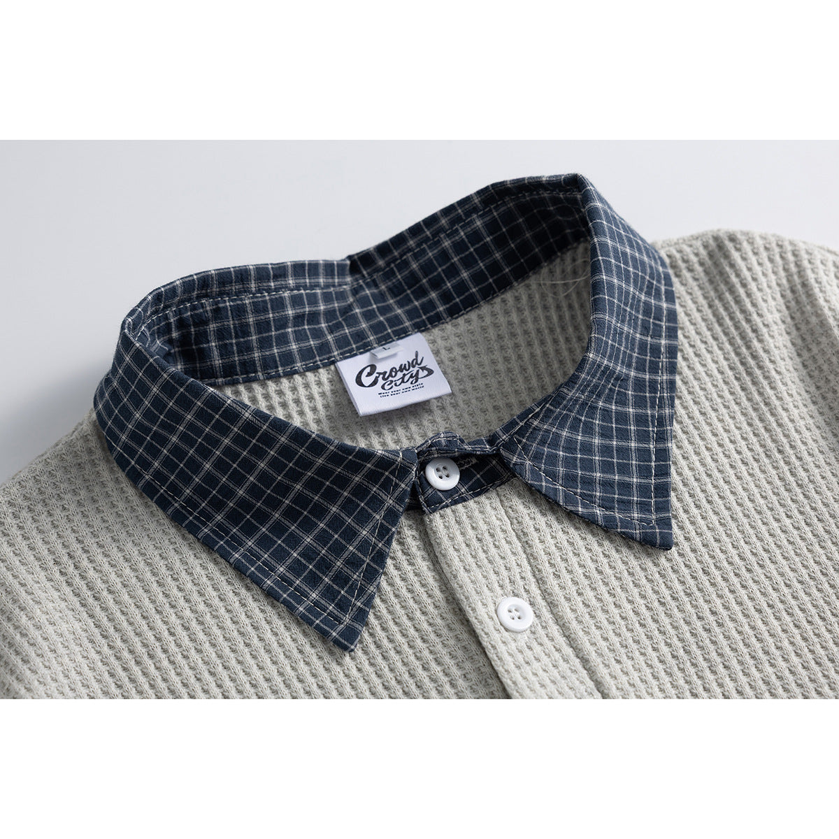 Close-up of a light gray textured polo with a navy plaid collar and white buttons.