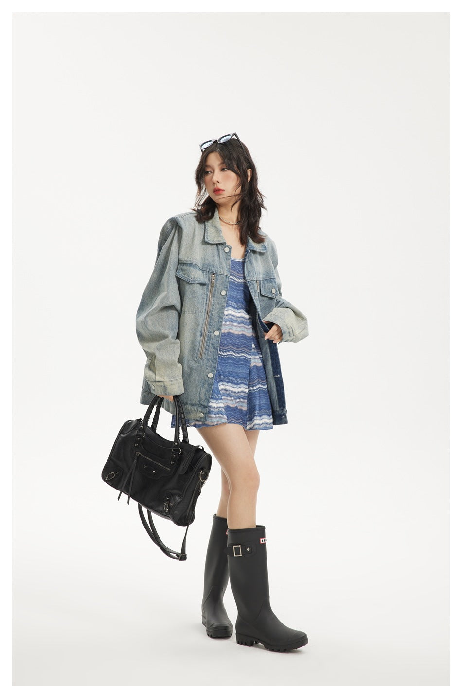 Model wearing an oversized washed blue denim jacket open over a blue patterned dress with black boots and a black bag