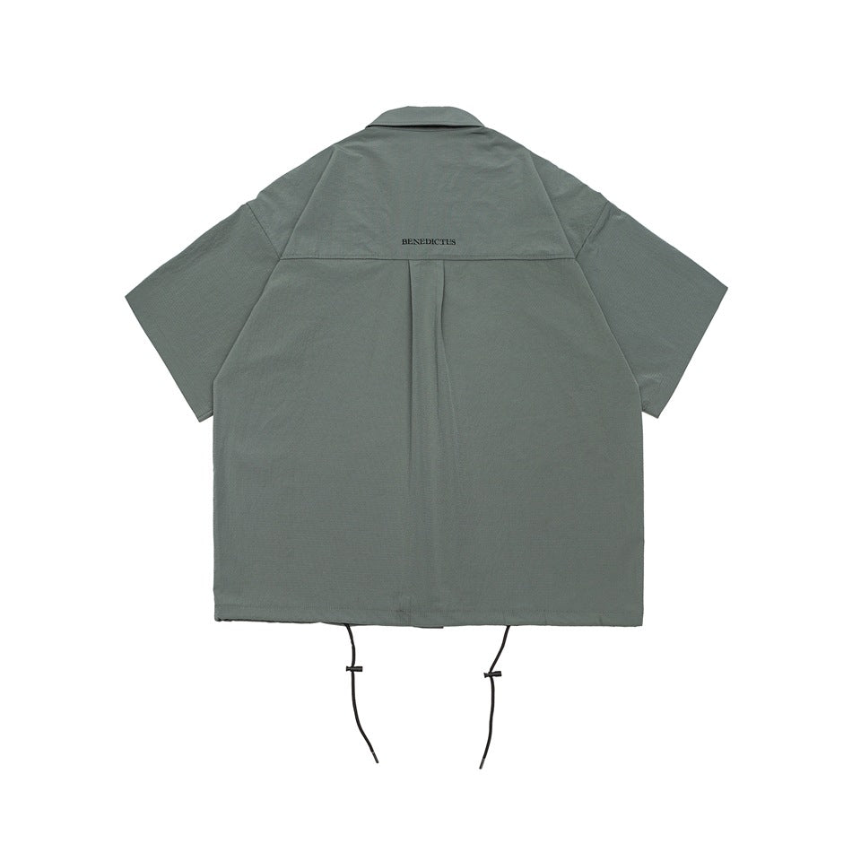 Back of gray-green short-sleeve shirt with yoke seam, center pleat, small embroidered text and drawstring hem