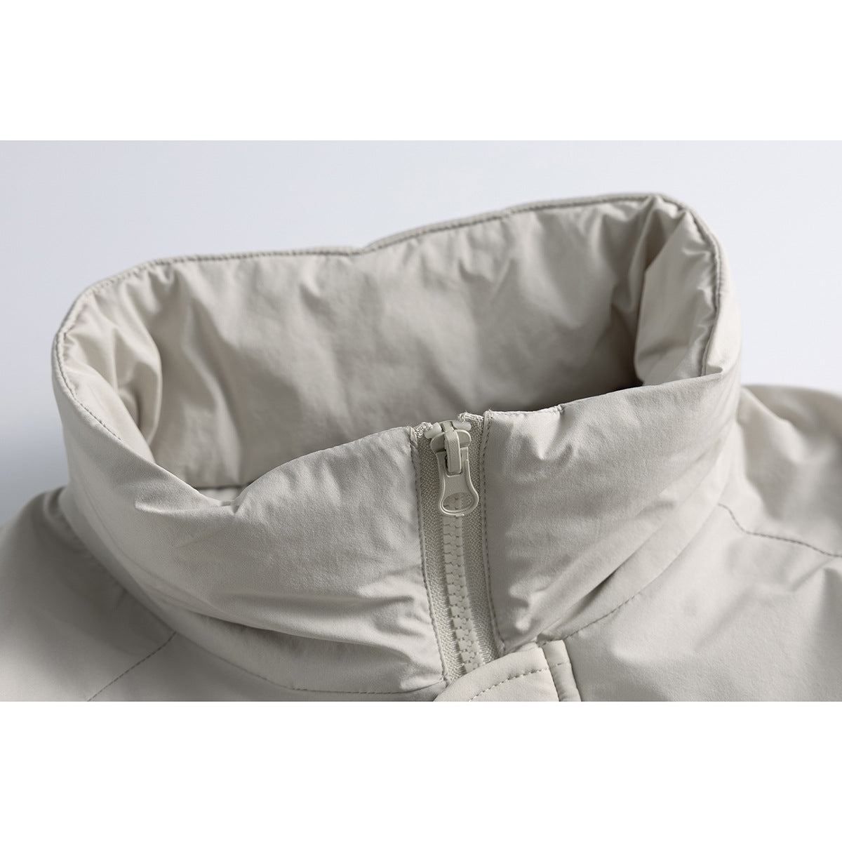 Close-up of a light gray jacket’s tall collar and matching front zipper.