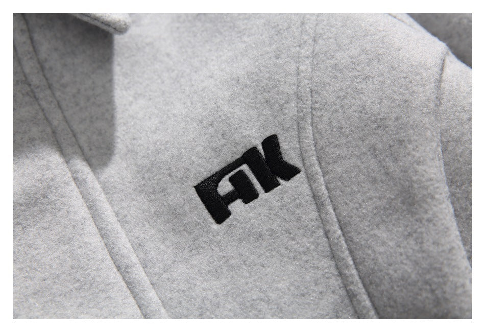Close-up of a black embroidered emblem on the light gray jacket, showing the surrounding seam and textured surface.