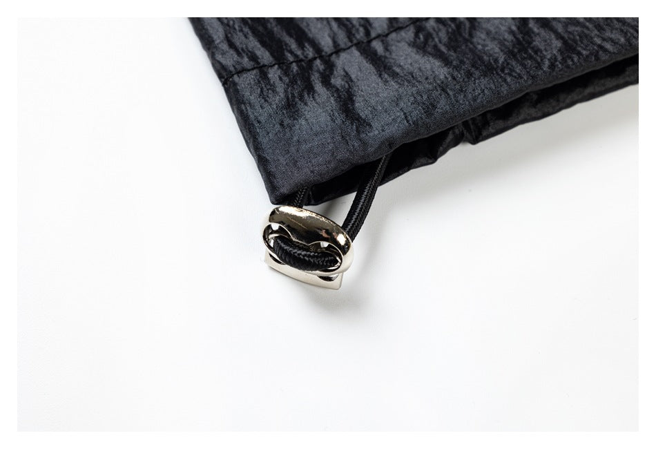 Close-up of a black garment edge with a black drawcord threaded through a shiny metal toggle.