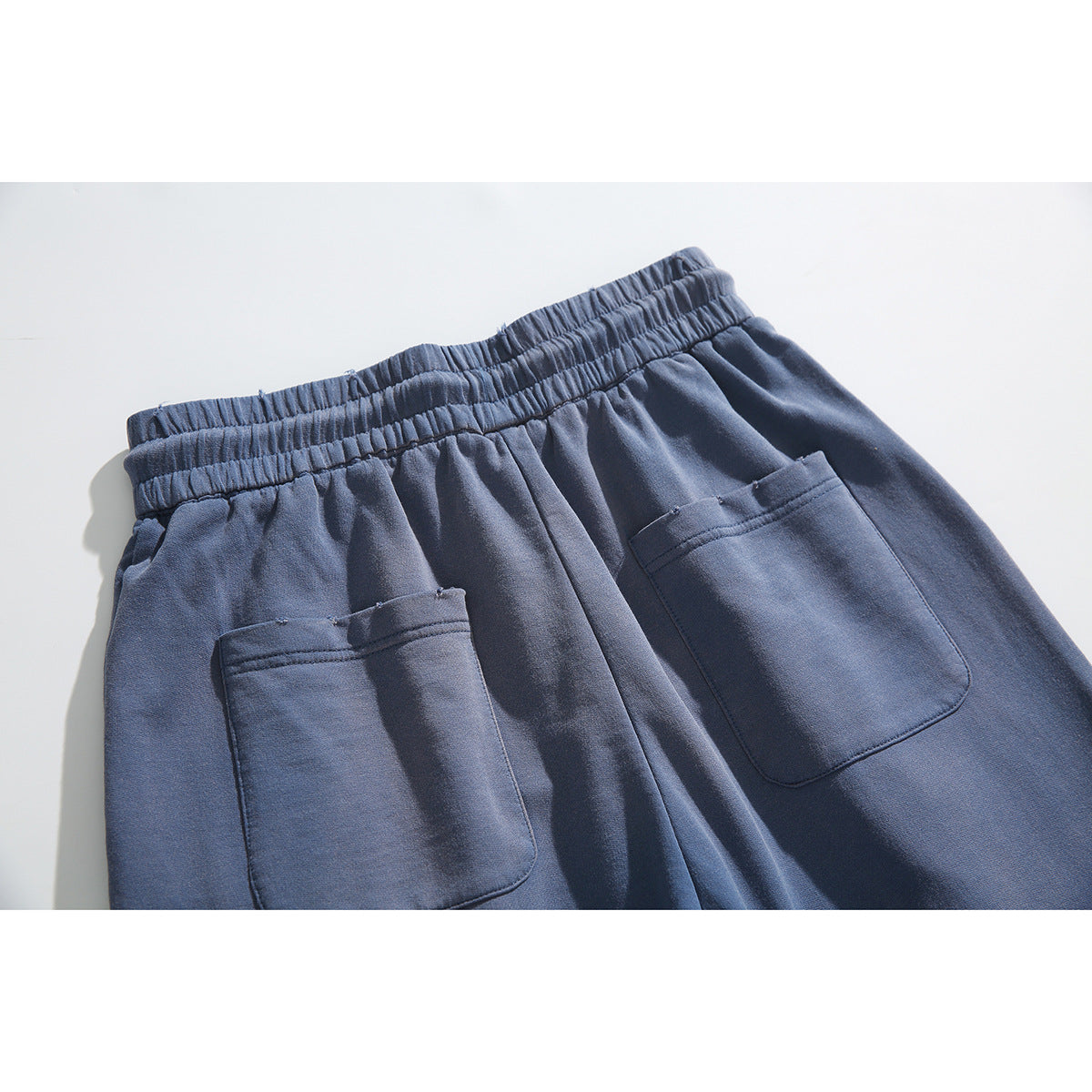 Close-up of the back of slate-blue pants, showing an elastic waistband and two patch pockets.