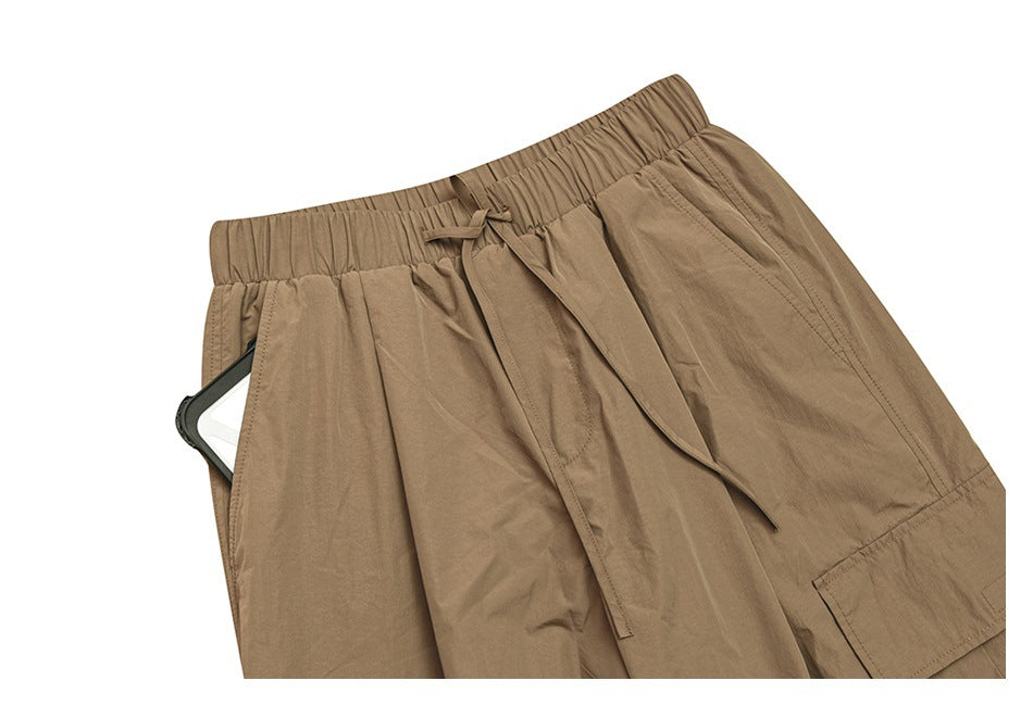 Close view of tan trousers showing the elastic drawstring waist, front pocket and part of a cargo pocket.