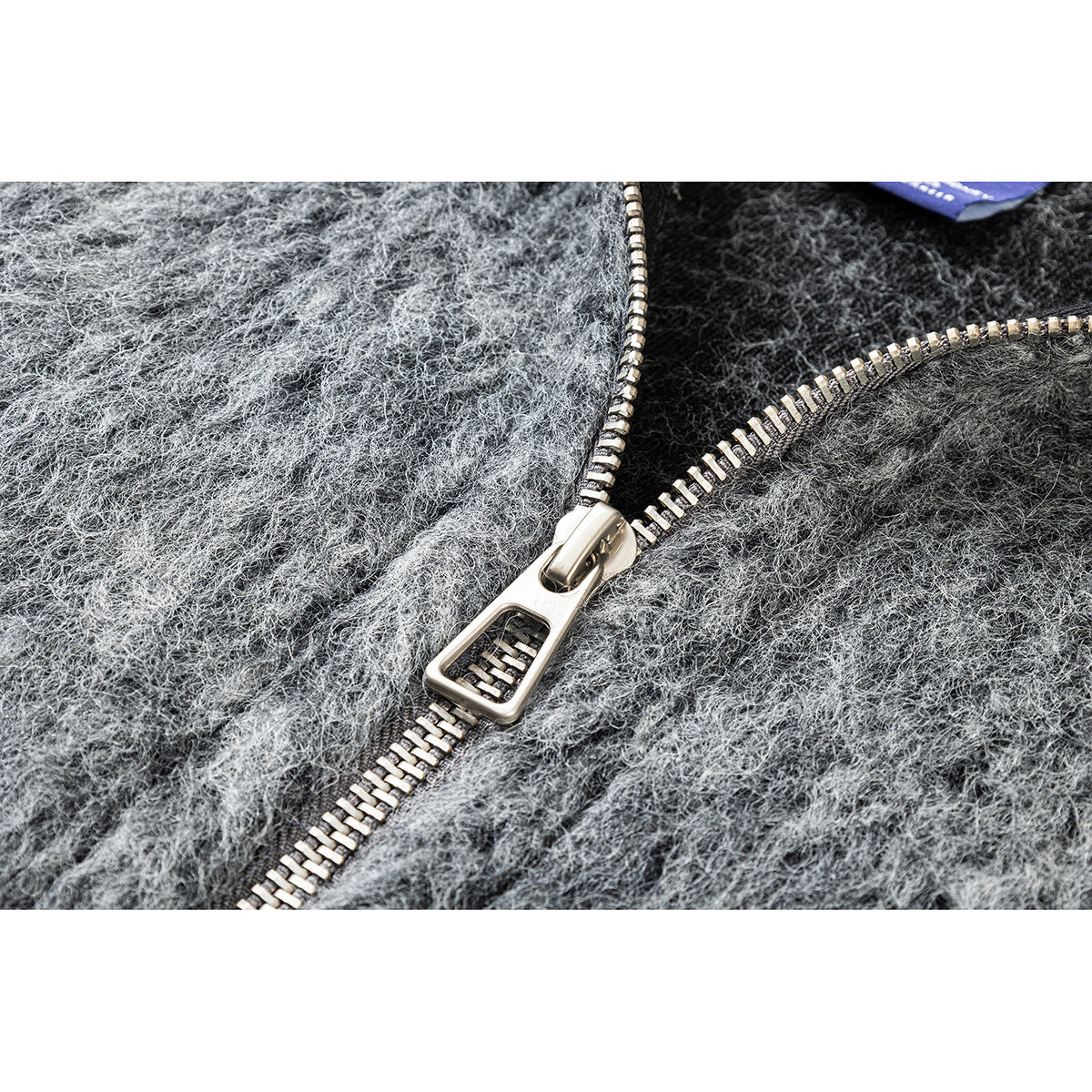 Close-up of a chunky silver zipper on a fuzzy heather-gray jacket.