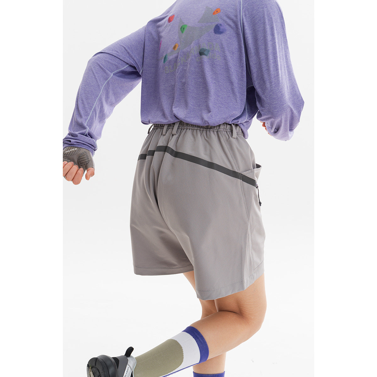Rear three-quarter view of a model wearing light gray shorts with a dark diagonal rear pocket zipper.