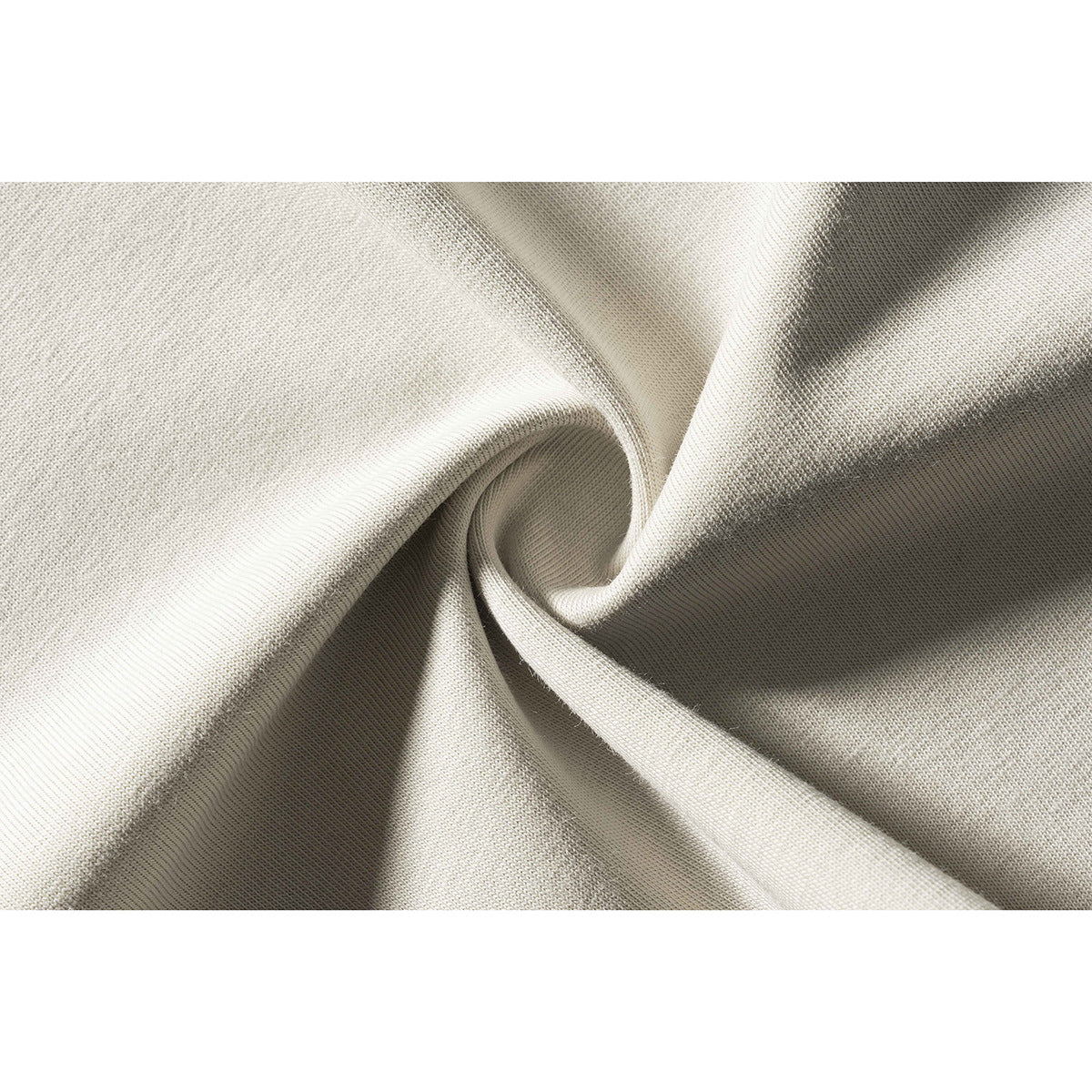 Close-up of light beige knit fabric arranged in soft folds, showing its surface texture.
