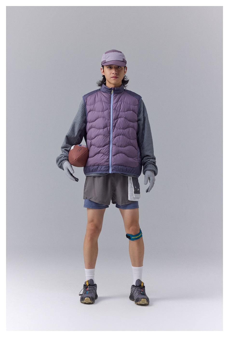 Model wearing a mauve quilted vest with dark trim over a gray textured top and layered gray-blue shorts.
