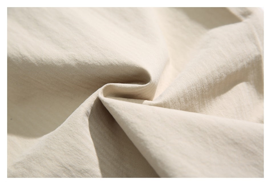 Close-up of beige garment fabric gathered into soft folds, showing its surface texture.