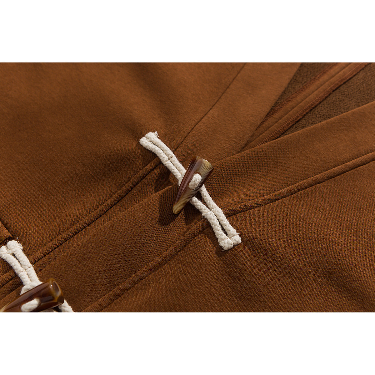 Close-up of a rust-brown jacket's front with cream rope-and-toggle closures.