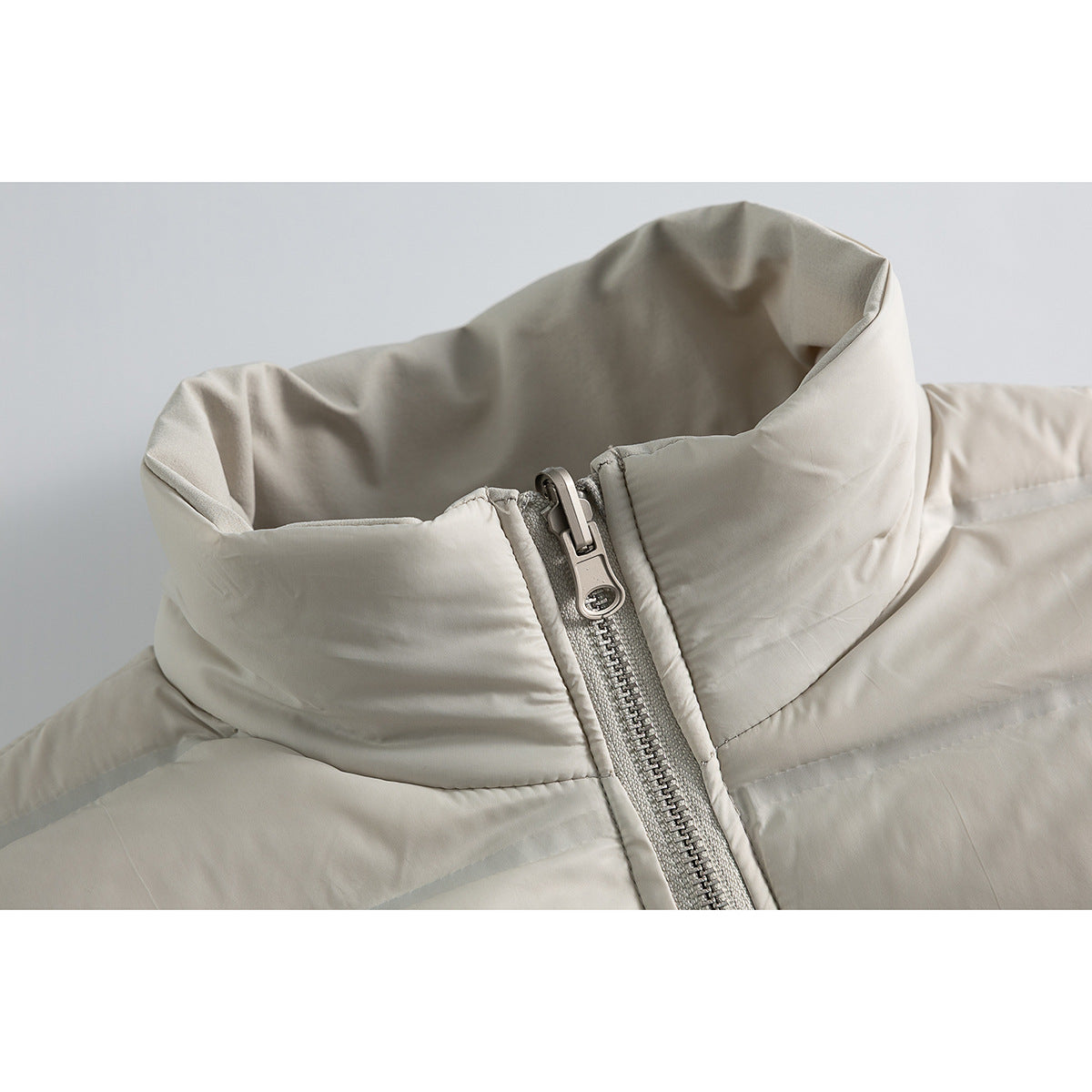 Close-up of a light gray jacket's tall padded collar and central silver zipper.