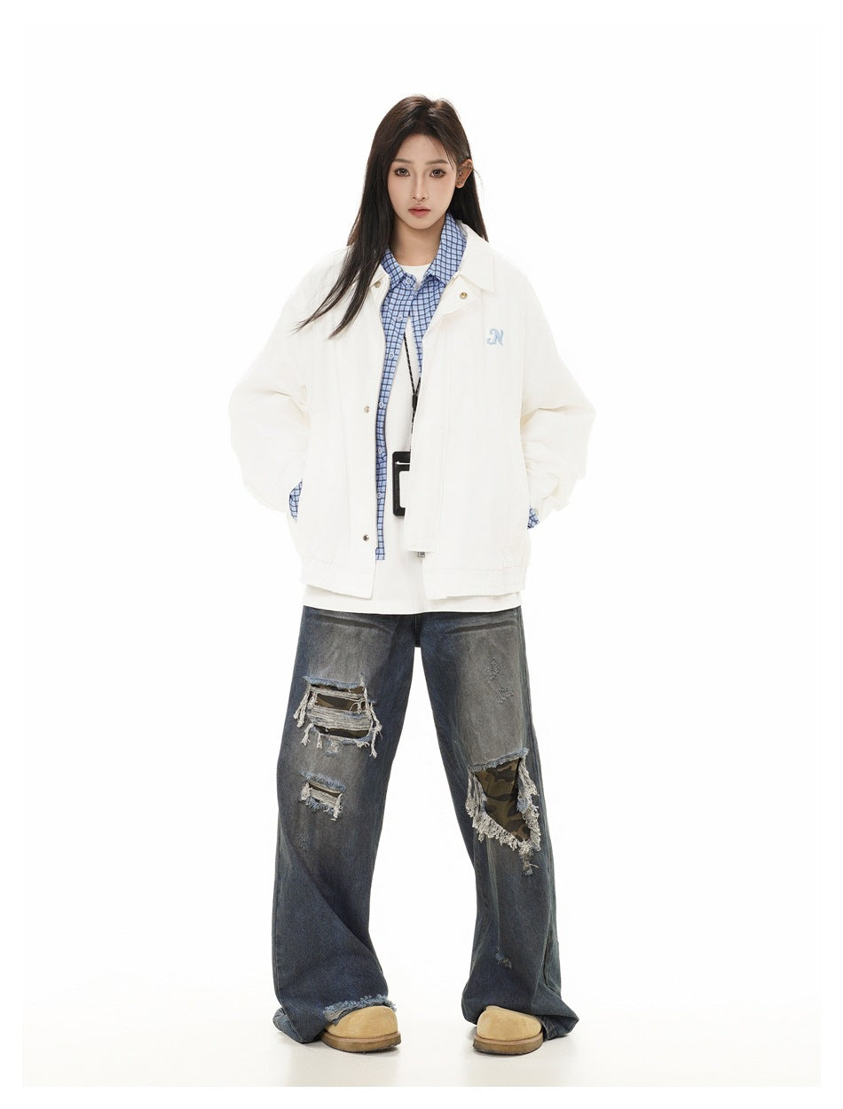 Full-length view of a model wearing a white oversized jacket with blue checked trim and distressed wide-leg jeans.