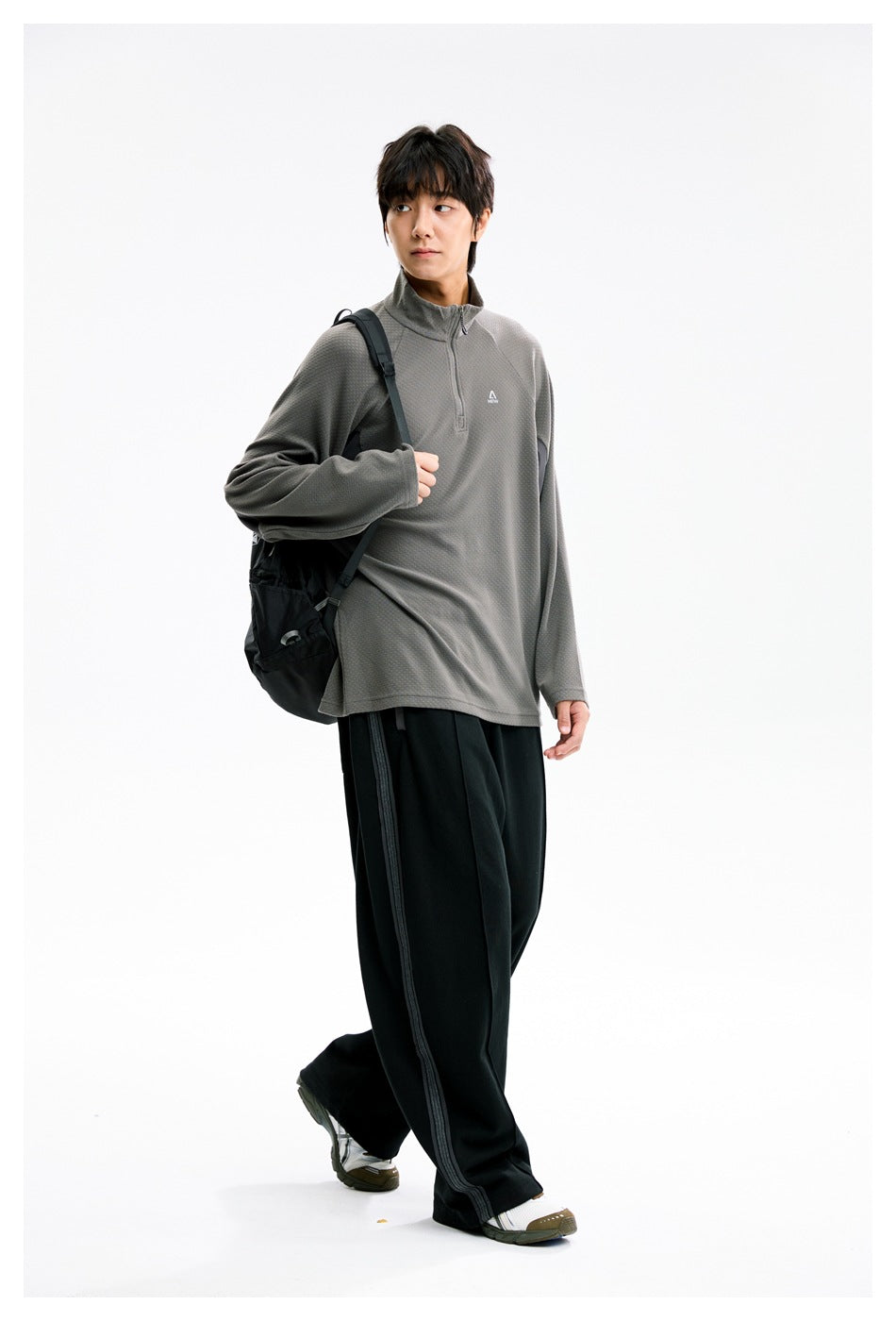 Model walking in a gray half-zip pullover with black side-striped wide-leg pants and a black backpack