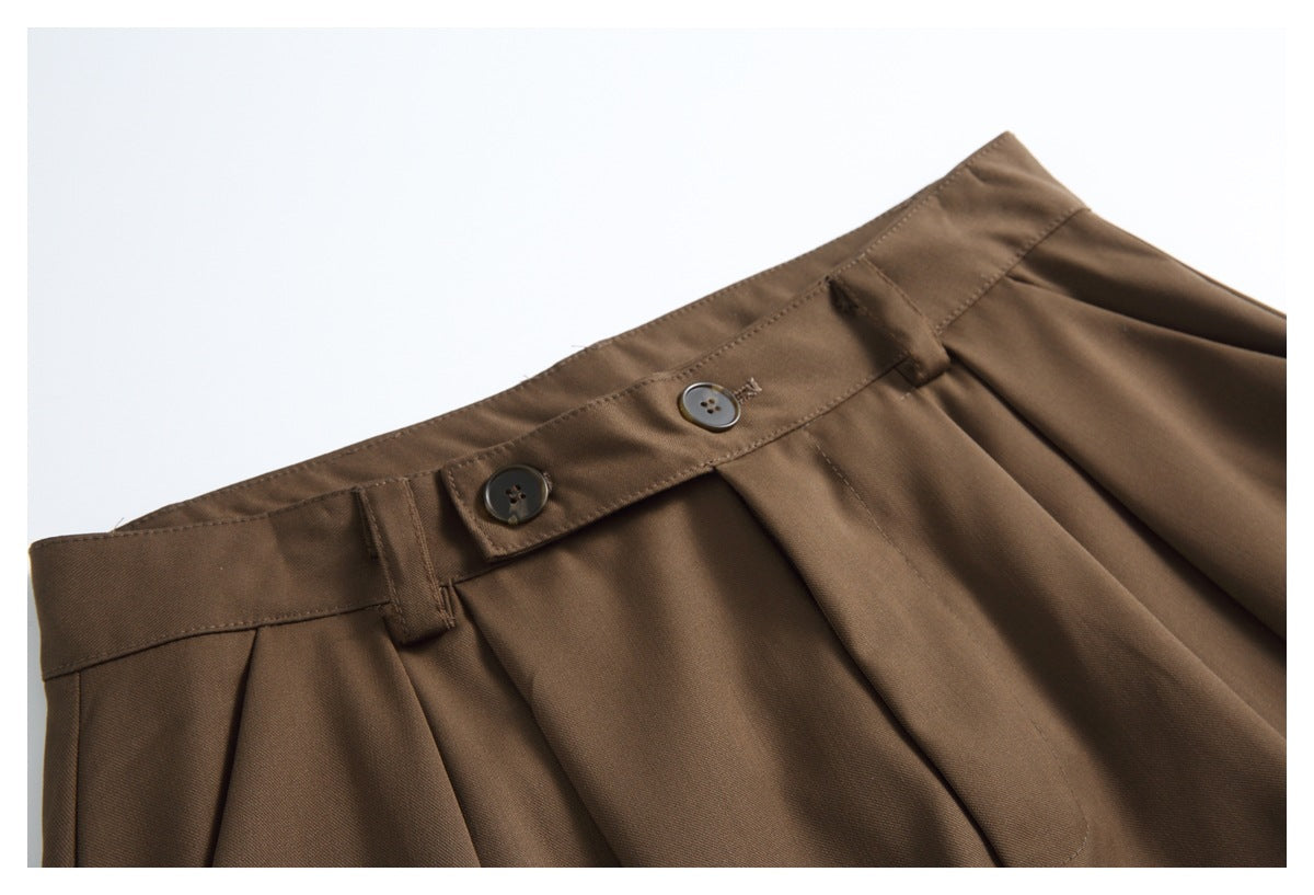 Close-up of brown shorts showing the waistband, two buttons, belt loops and front pleats.