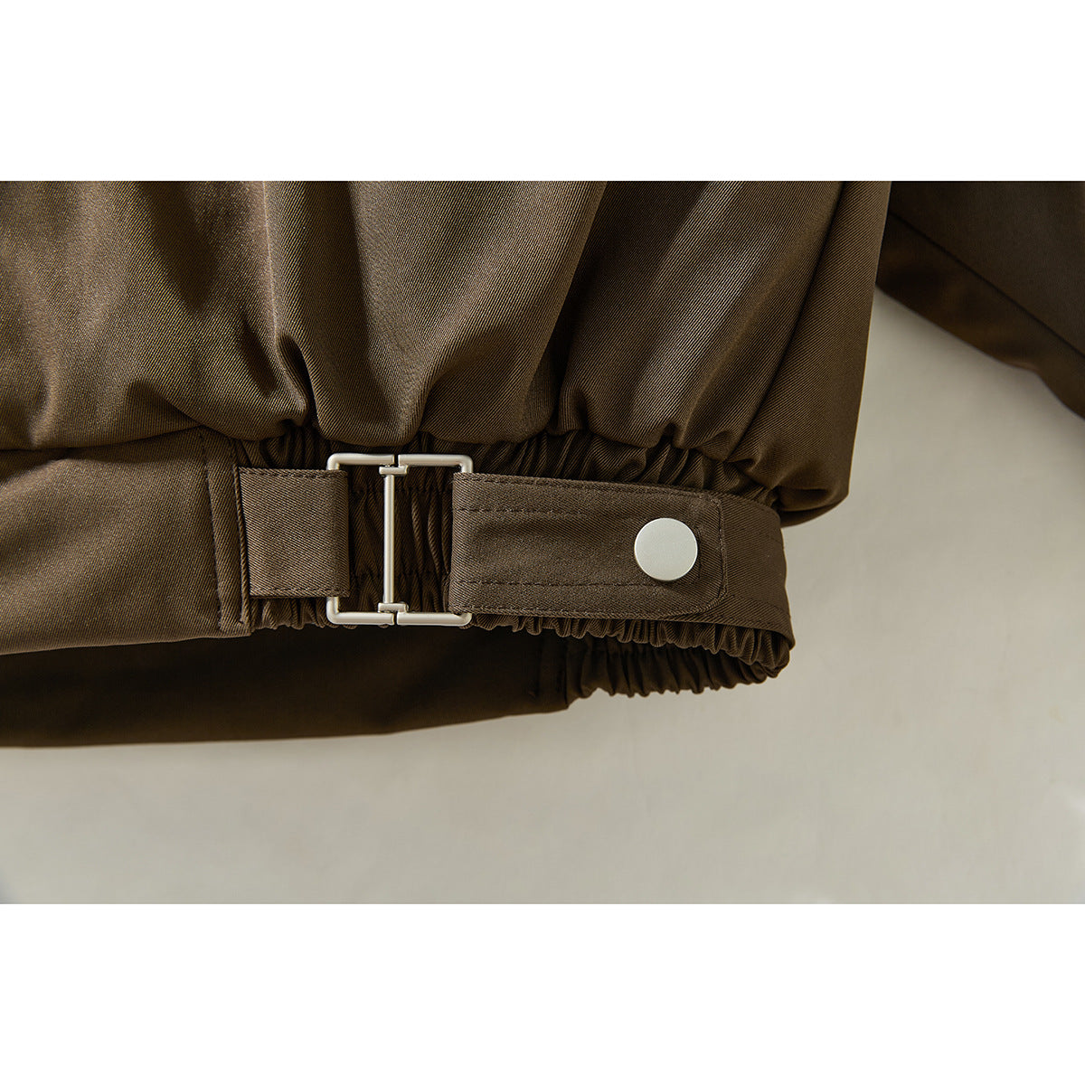 Close-up of the dark brown jacket's gathered hem and adjustable buckle strap.