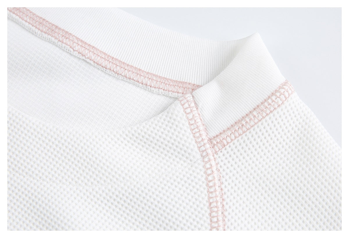 Close-up of the white ribbed crew neckline and shoulder seams with pale pink stitching.