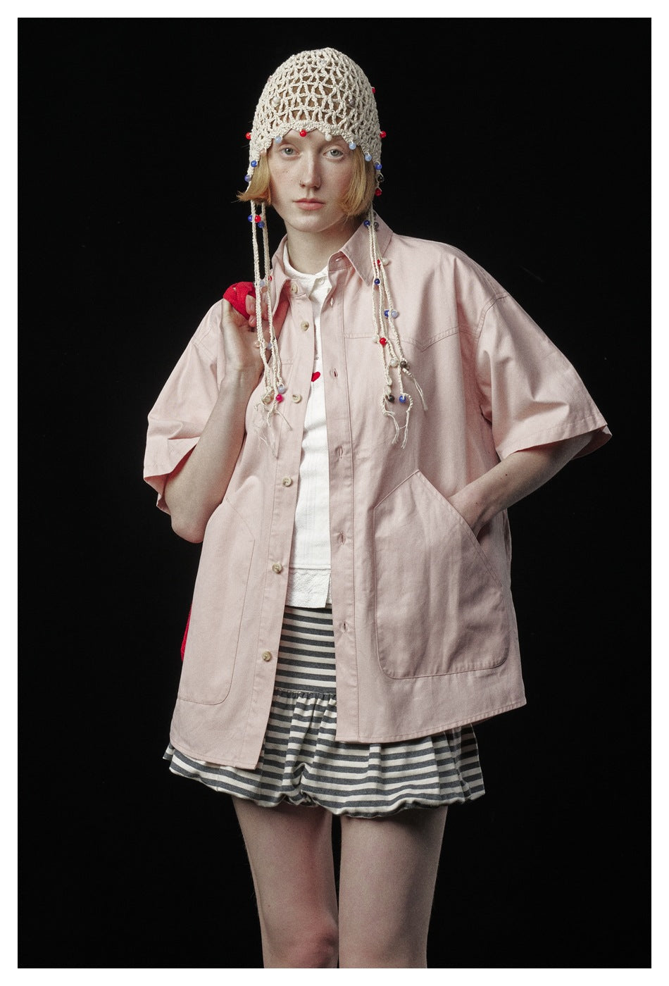 Model wearing a pale pink oversized short-sleeve button-up shirt with two large pockets and striped shorts.