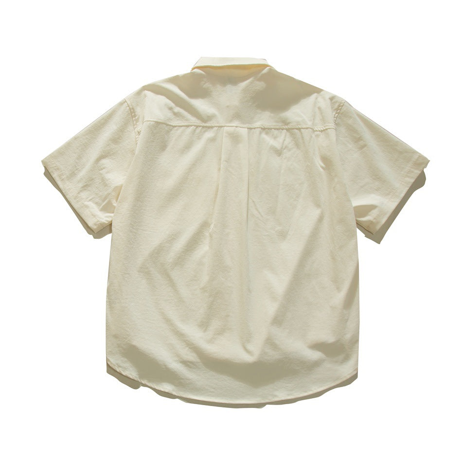 Back view of an ivory short-sleeve button-up shirt, with a yoke seam and center pleat.