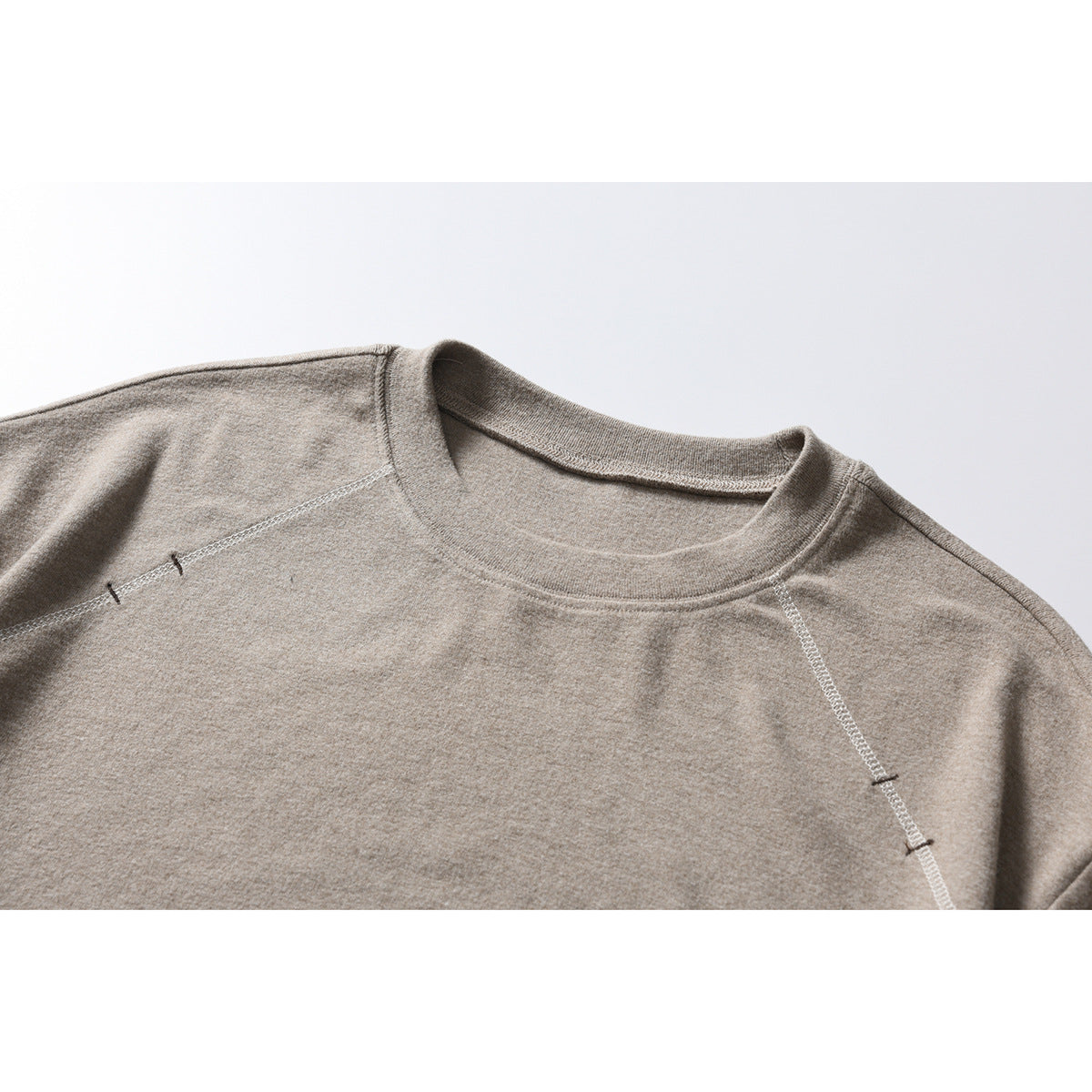 Close-up of a taupe crewneck sweatshirt showing the collar and raglan shoulder seams.