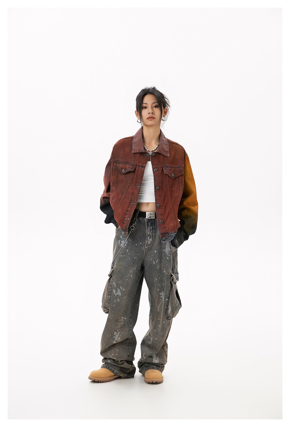 Full-length front view of a model wearing a rust-red color-block denim jacket and loose splatter-print gray cargo jeans.
