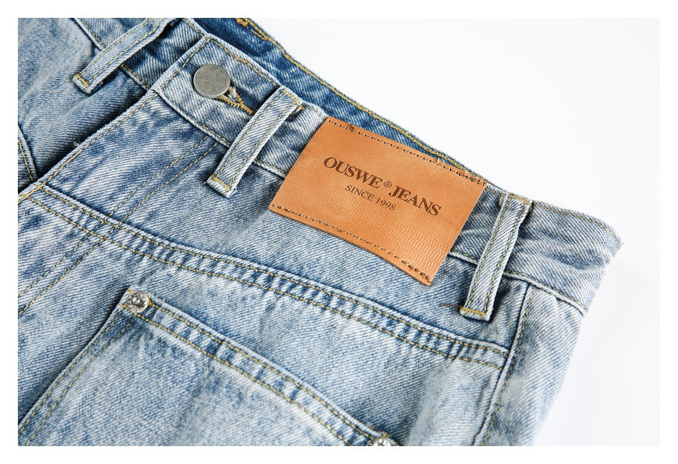Close-up of light blue jeans waistband, belt loops, button, pocket and a tan OUSWE JEANS patch.