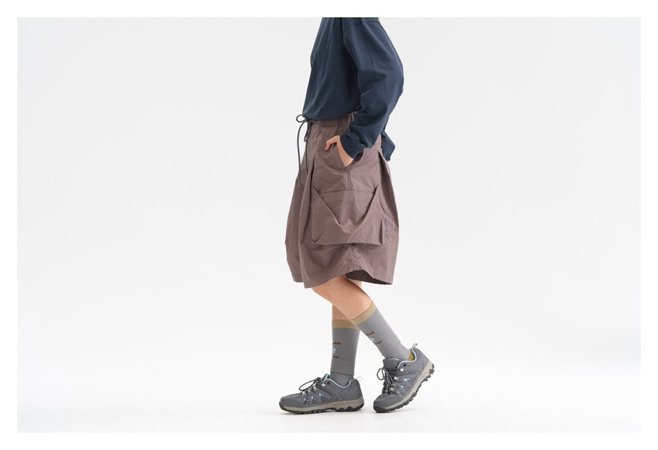 Side view of a model wearing mauve-gray wide cargo shorts with a large side pocket and drawstring waist.