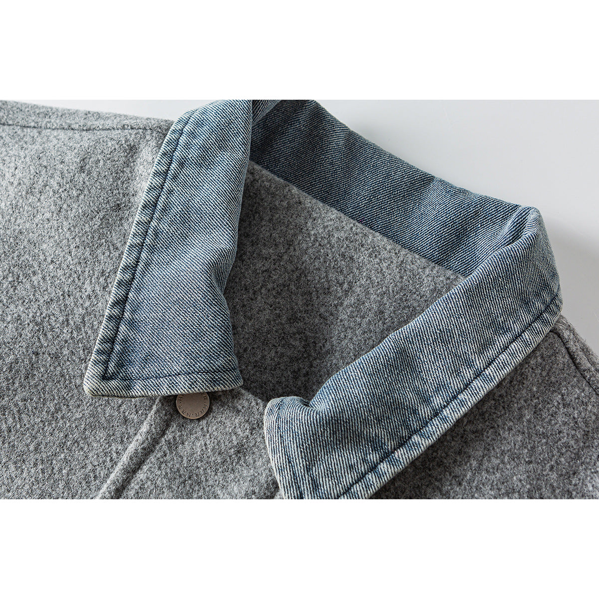 Close-up of a gray jacket with a blue denim collar facing and a small metal button.